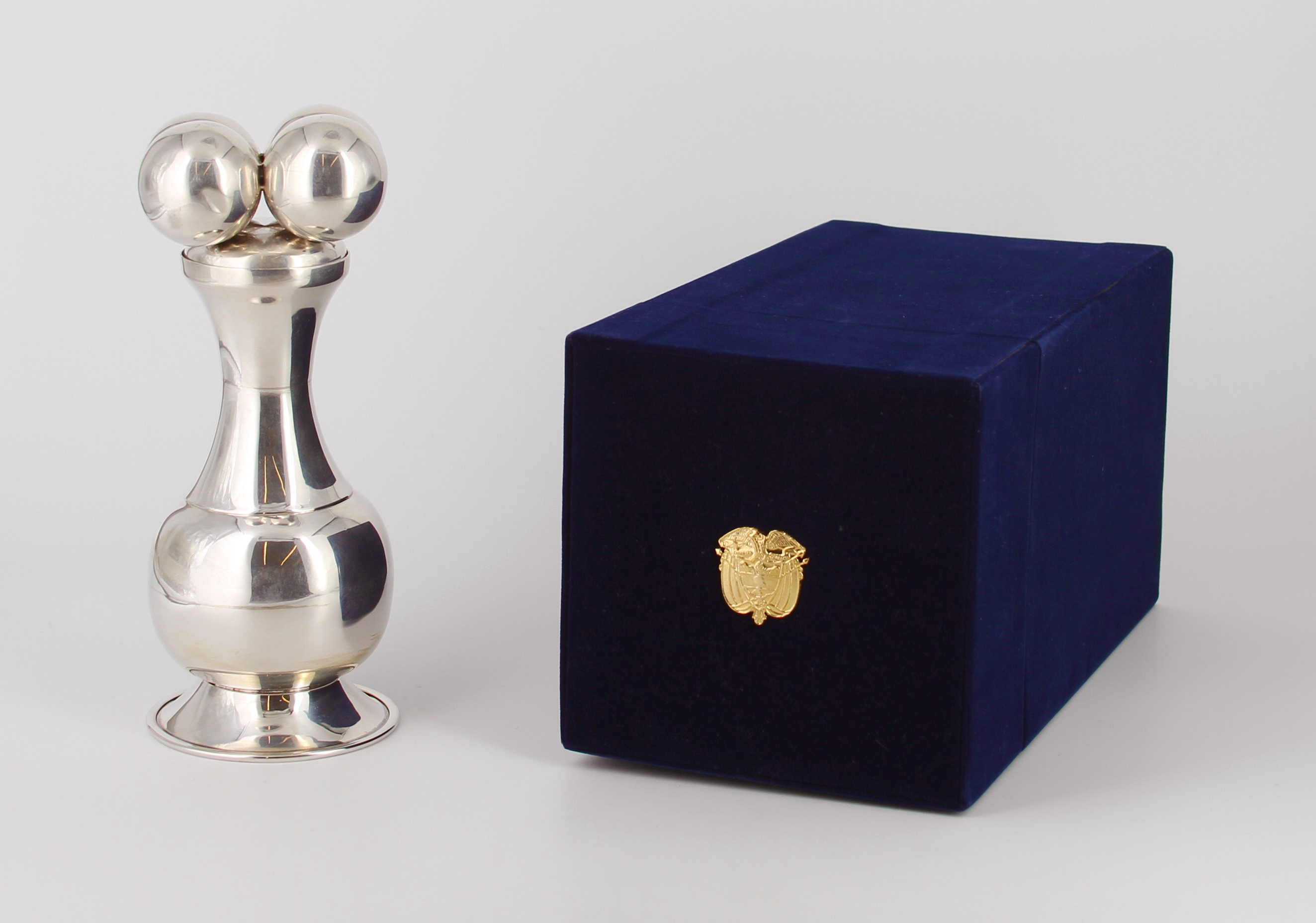 Silver container with removable lid that represents an indigenous artifact; held in a blue velvet hinged box with the coat of arms of Colombia on the lid. Presented to President Bush during a working visit to Washington, D. C. in 2007. Gifted by Alvaro Uribe, President of the Republic of Colombia.