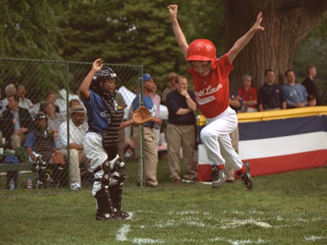A tee ball player leaps in the air as he crosses home.